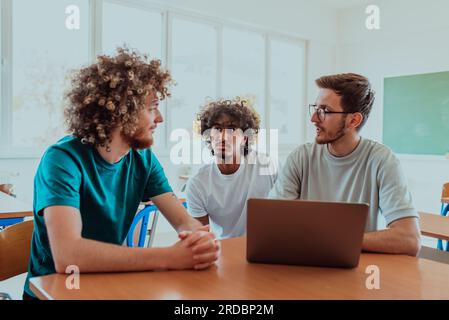 Raggruppare gli studenti, tra cui un afro-americano, seduti insieme in classe, impegnati in una discussione mentre esaminano le informazioni su un notebook Foto Stock