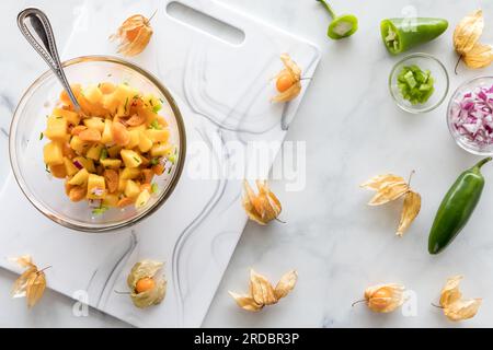 Una ciotola di salsa di bacche dorate fatte in casa e mango circondata da ingredienti. Foto Stock