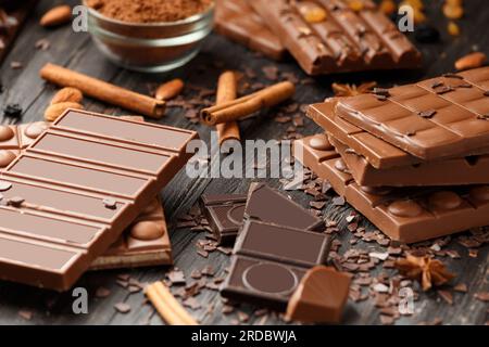 Cioccolato intero e rotto, barrette di cioccolato, caramelle, gocce di cioccolato su sfondo di legno scuro Foto Stock