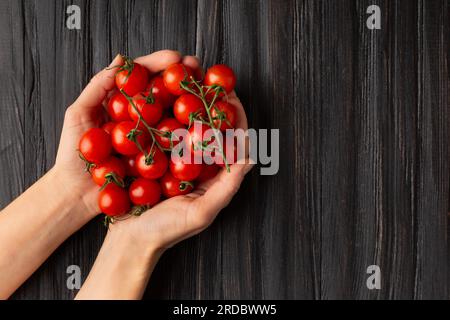 Pomodori ciliegini a mani su fondo di legno con posto per testo, vista dall'alto . Una manciata di pomodori freschi nelle palme femminili. Foto Stock