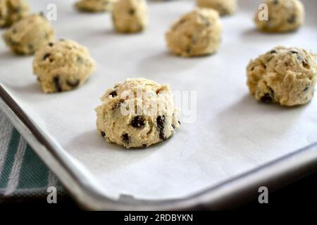 Cucchiai di impasto di biscotti con gocce di cioccolato su una teglia da forno rivestita di carta pergamena Foto Stock