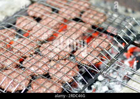 Polpette alla griglia kofta kufta di carne macinata di manzo in una rete a rete grigliata con manico su un carbone con fuoco e fuoco alla griglia, barbecue succoso Foto Stock