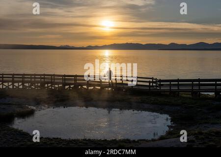 Uomo in piedi che guarda Lakeside Spring mentre il sole sorge dietro il lago Yellowstone, West Thumb, Yellowstone National Park, Montana Foto Stock