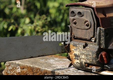 Vecchia macchina per il taglio del legno a benzina con vista sullo scarico arrugginito del motore. Motosega rugginita all'aperto Foto Stock