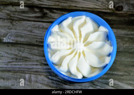 gelato alla vaniglia bianco congelato in un recipiente di plastica isolato su fondo di legno e pronto per essere servito, un gelato alla vaniglia a forma di fiore in blu c Foto Stock