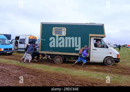 Persone che spingono un camion, un veicolo, bloccati in un campo fangoso al Tropical Pressure Festival in Cornovaglia, Regno Unito Foto Stock