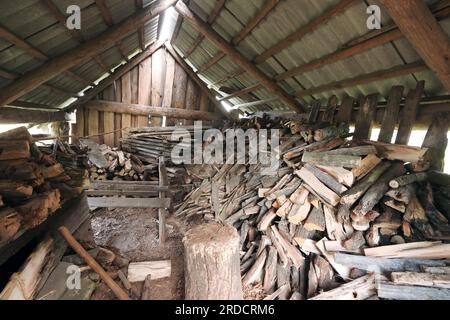 Legna da ardere tagliata in un vecchio fienile. Piegato in modo ordinato. È visibile un ponte per tagliare la legna da ardere. Foto Stock