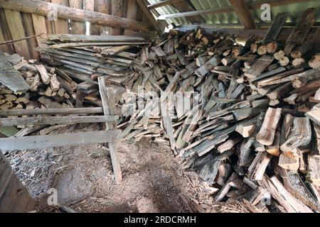 Legna da ardere tagliata in un vecchio fienile. Piegato in modo ordinato. Potete vedere un dispositivo per tagliare la legna da ardere. Foto Stock