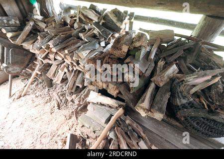 Legna da ardere tagliata in un vecchio fienile. Piegato in modo ordinato. Potete vedere un dispositivo per tagliare la legna da ardere. Foto Stock