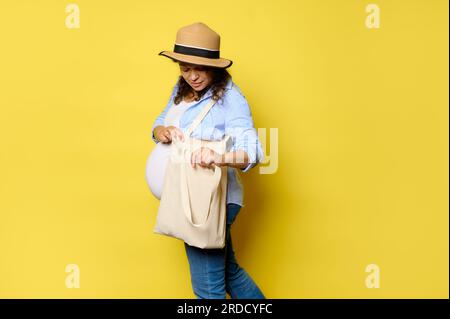 Ritratto di un'affascinante donna incinta che usa una borsa per la spesa in lino, isolata su sfondo giallo con spazio pubblicitario. Persone. Stile di vita sostenibile. E Foto Stock