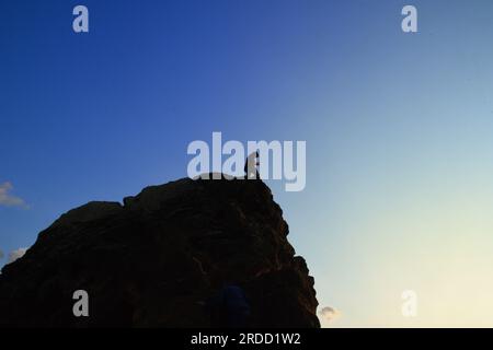 Silhouette di un giovane che guarda in basso da una grande roccia. Foto Stock