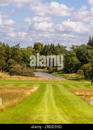 Ampio sentiero in erba falciata che conduce attraverso l'erba lunga e selvaggia fino al lago Arboretum in lontananza. North Yorkshire. REGNO UNITO Foto Stock