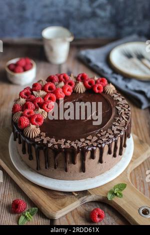 Torta di lamponi al cioccolato con ganache al cioccolato e lamponi freschi in cima. Tagliere di legno. Sfondo blu. Foto Stock