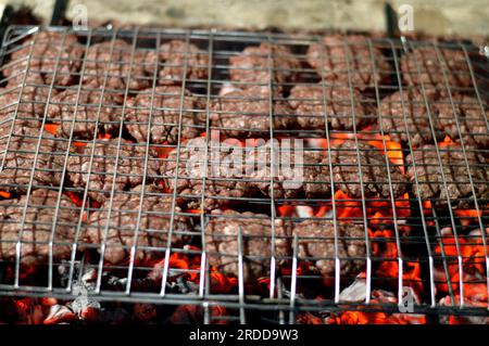 Polpette alla griglia kofta kufta di carne macinata di manzo in una rete a rete grigliata con manico su un carbone con fuoco e fuoco alla griglia, barbecue succoso Foto Stock