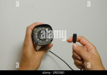 Mani esperte che lavorano alla manutenzione di una telecamera di sicurezza bianca, sottolineando il concetto di protezione e sorveglianza. Foto Stock