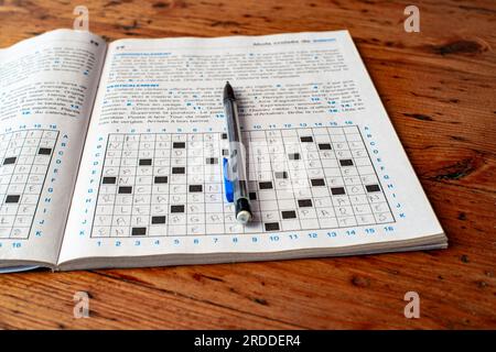 Libro degli esercizi del puzzle della parola crociata francese. Il libro si trova su un tavolo di legno di colore rosso. La matita si trova sul notebook. Foto Stock