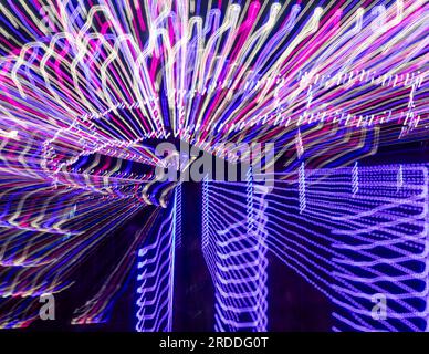 Giro di divertimento di notte, lunga esposizione nel movimento della fotocamera, motivo astratto di strisce chiare rosa, viola e blu su sfondo scuro Foto Stock