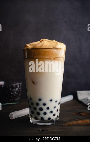 Caffè Dalgona freddo con Boba in una pinta di vetro su sfondo scuro: Caffè dalgona freddo con latte e perle di tapioca mostrate con una paglia di boba Foto Stock