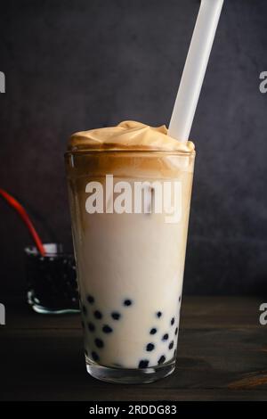 Caffè Dalgona freddo con Boba in una pinta di vetro su sfondo scuro: Caffè dalgona freddo con latte e perle di tapioca mostrate con una paglia di boba Foto Stock