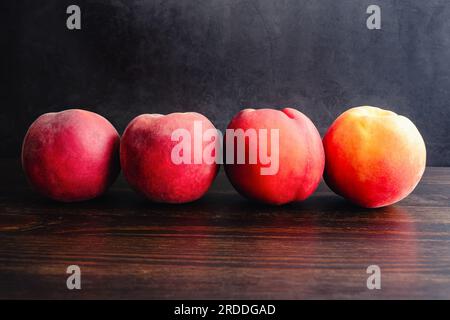 Fila di quattro pesche su tavola di legno: Pesche fresche raggruppate su sfondo scuro Foto Stock