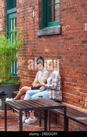 Giovani coppie al riparo da una leggera doccia a pioggia nel quartiere storico della distilleria di Toronto, Ontario, Canada Foto Stock