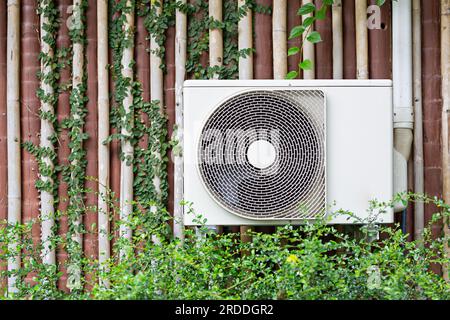 L'aria condizionata è montata sulla parete con gli alberi dell'edificio e il giardino in prima fila. Foto Stock