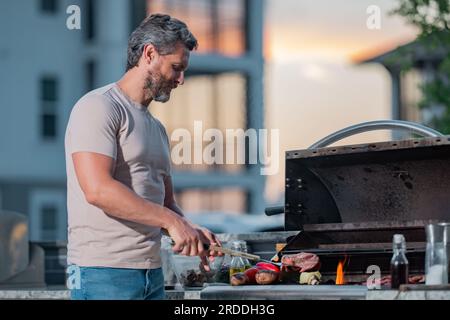 Maestro del barbecue uomo ispanico di mezza età in grembiule per arrostire  barbecue e grigliare uomo tenere cookin