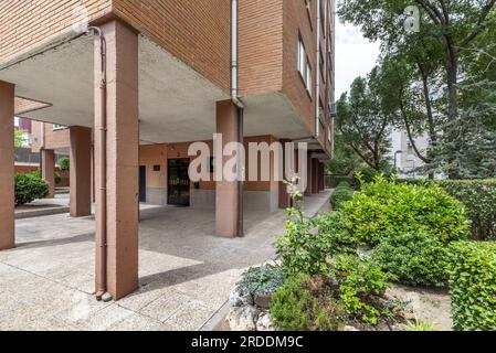 Aree comuni di un edificio residenziale urbano con siepi rifinite, grandi alberi e un portale di accesso di porte metalliche nere Foto Stock