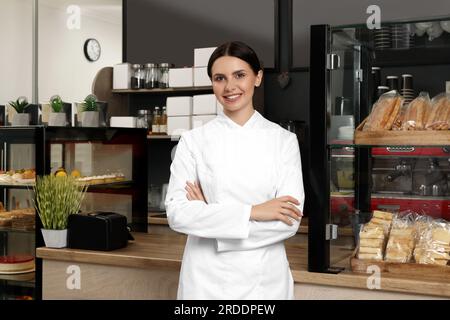 Ritratto di Happy baker vicino a una vetrina con pasticcini nel suo caffè Foto Stock