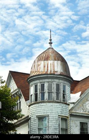 La torre rotonda ha una parte superiore a cupola e una finitura in metallo. La casa è bianca, con i lati a ciottoli, la vernice si stacca e la finestra rotta. Home si trova a Hancock, Michigan Foto Stock