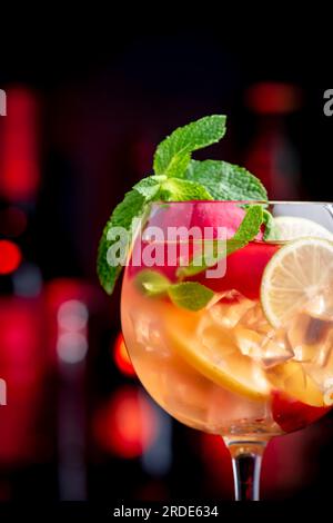 Sangria rosa bevanda alcolica estiva con vino rosa, pesca, arancia, lime e ghiaccio. Sfondo nero bar, utensili da bar in acciaio e bottiglie Foto Stock