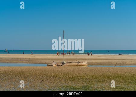 Costa da Morondava con una barca in legno di baobab con bassa marea sulla sabbia, sfondo con la gente Foto Stock