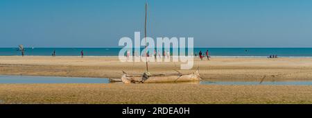 Costa da Morondava con una barca in legno di baobab con bassa marea sulla sabbia, sfondo con panorama delle persone Foto Stock