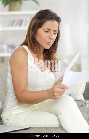 scioccata la giovane donna che legge una lettera mentre tocca la testa a casa Foto Stock