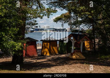 Spogliatoi sulla spiaggia dell'isola di Pihlajasaari con Länsiterminaali 2 o Terminal 2 ovest di Länsisatama o Jätkäsaari sullo sfondo a Helsinki, Finlandia Foto Stock