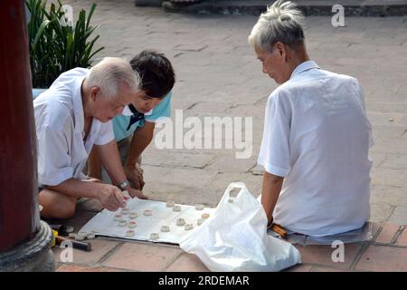 Gli uomini più anziani giocano scacchi vietnamiti all'esterno di un tempio chiamato Ngọc Sơn Temple , in vietnamita: Đền Ngọc Sơn, chữ Nôm: 𪽛玉山, situato su un isolotto nel lago Hoàn Kiếm, nel centro di Hanoi, in Vietnam, Asia; dedicato ai filosofi confuciani e taoisti e all'eroe nazionale, Trần Hưng Đạo, Foto Stock