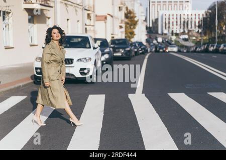 Giovane donna che cammina su un incrocio per strada attraverso la città autunnale Foto Stock