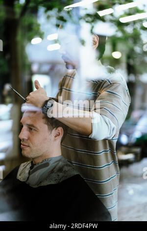 Un barbiere giapponese taglia i capelli di un cliente uomo in un barbiere. Foto Stock