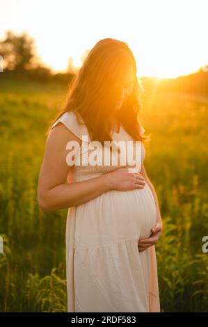 Foto di maternità di una mamma incinta che tiene il batto del bambino all'aperto in natura Foto Stock