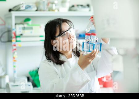 giovane scienziata donna che controlla una provetta di un rack Foto Stock