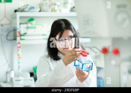 giovane scienziata donna che controlla una provetta in un rack Foto Stock