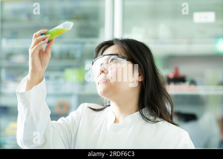 giovane scienziata cinese femmina che controlla un campione in un tubo Foto Stock