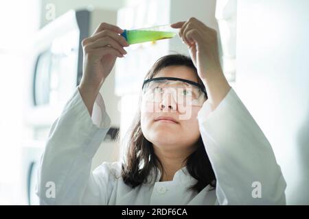 giovane scienziata donna che controlla un liquore verde in tubetto Foto Stock