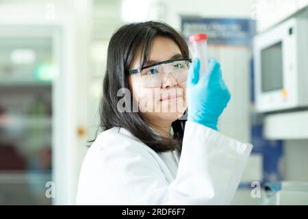 giovane scienziata cinese femmina che controlla un campione in un tubo Foto Stock