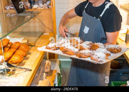 Inriconoscibile panettiere in bottega di panificio artigianale e bottega che mette croissant e napoletani Foto Stock