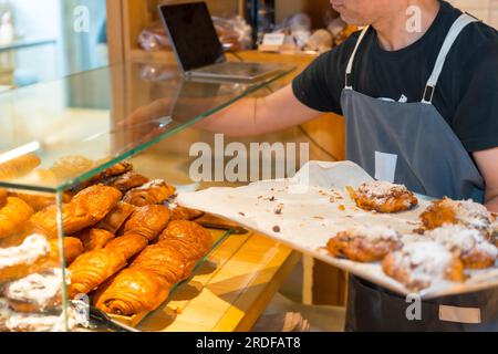 Inriconoscibile panettiere in bottega di panificio artigianale e bottega che mette croissant e napoletani Foto Stock