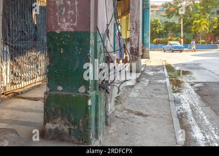 L'Avana, Cuba - 27 maggio 2023: Cavi elettrici disordinati che fuoriescono da una vecchia colonna in un portico di un edificio. In lontananza, una pozza d'acqua stagnante nel Foto Stock