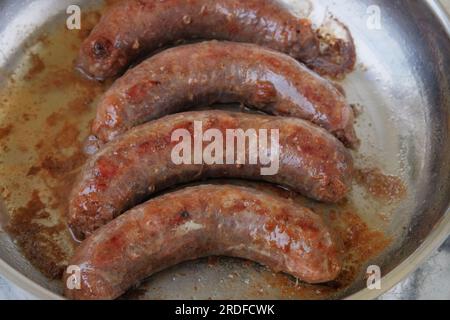 Le salsicce vengono fritte in una padella di metallo. Cibo fatto in casa. Cucinare a casa. Fast food. Foto Stock