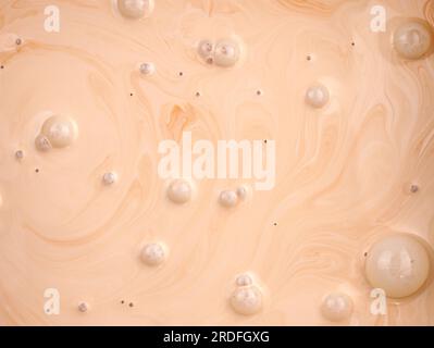 Vista dall'alto emulsione di vernice liquida con bolle. Primo piano di vernice per pareti color crema. Il processo di miscelazione della vernice a emulsione arancione e bianca. Foto Stock