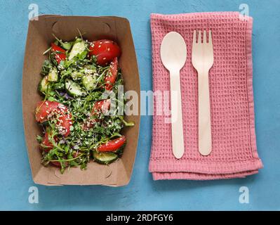 Vista dall'alto dell'insalata di verdure in una confezione di carta monouso. Insalata con pomodori, cetrioli e microgreen, cosparsa di semi di sesamo. Pink Kitchen towe Foto Stock